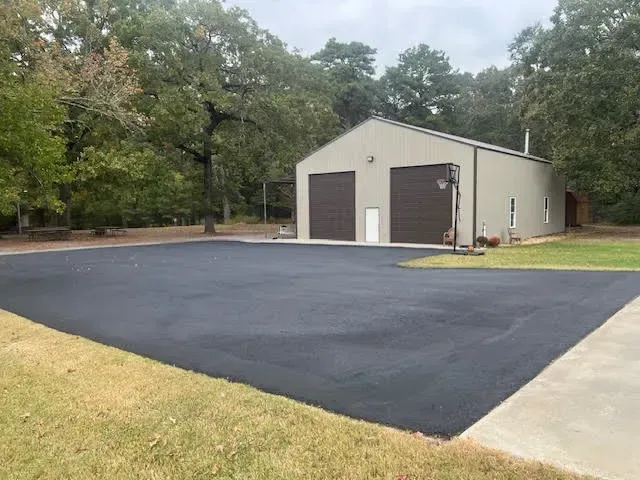 Asphalt driveway in front of a tan metal building with two brown garage doors. Trees in background.