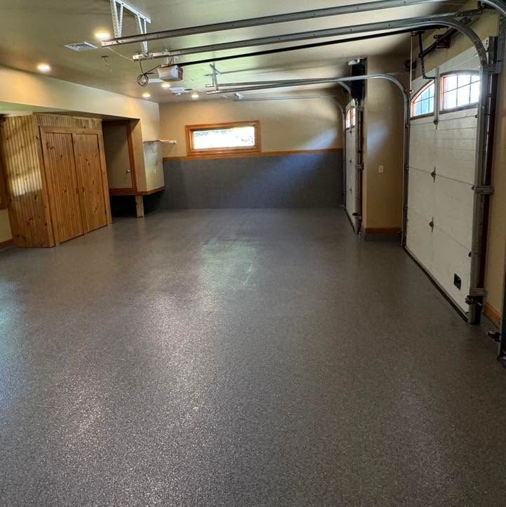Empty garage with gray epoxy floor, wood cabinets, windows, and overhead garage door