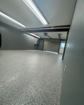 Empty garage interior with speckled floor, fluorescent lights, and an open garage door.