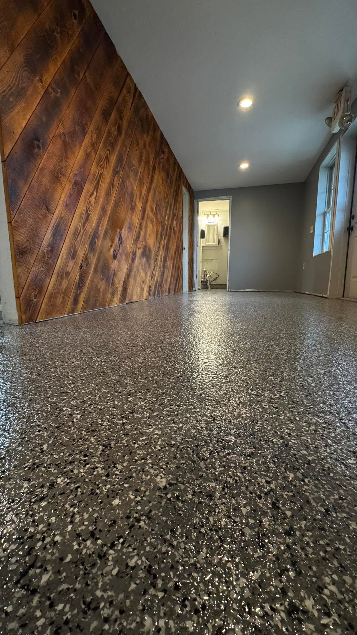 Empty hallway with glossy speckled floor, wood-paneled wall, and recessed ceiling lights