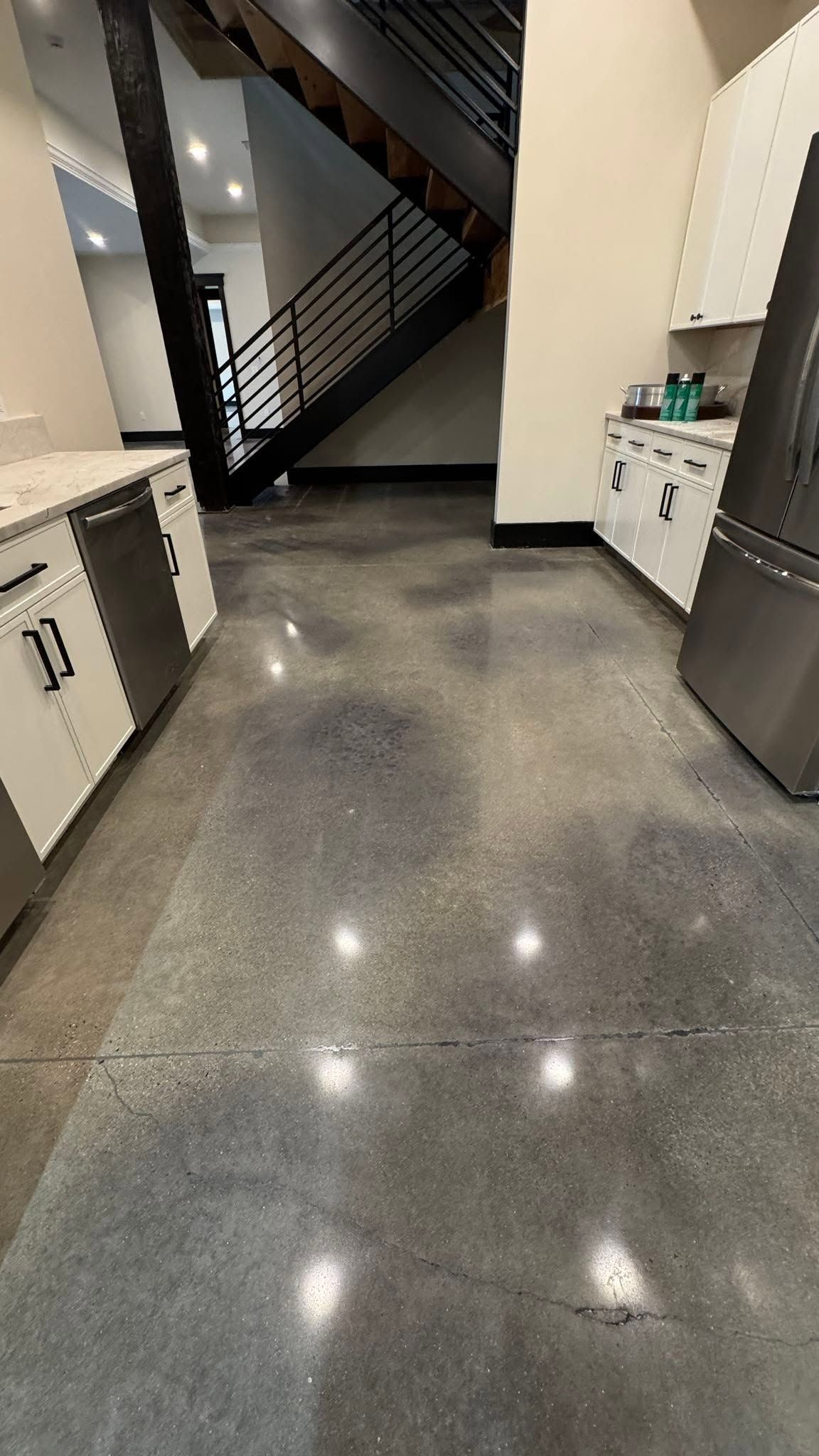 Modern kitchen with gray cabinets, polished concrete floor, and staircase in the background