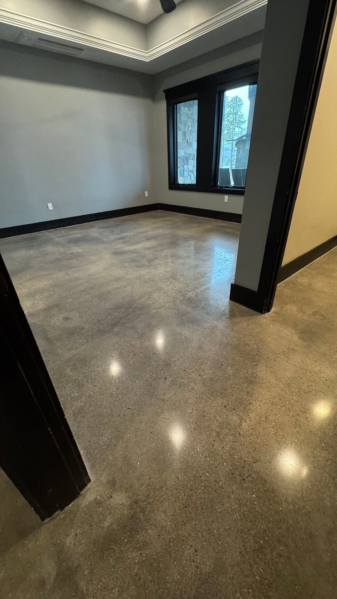Empty modern room with polished stone floor, gray walls, and large windows letting in daylight