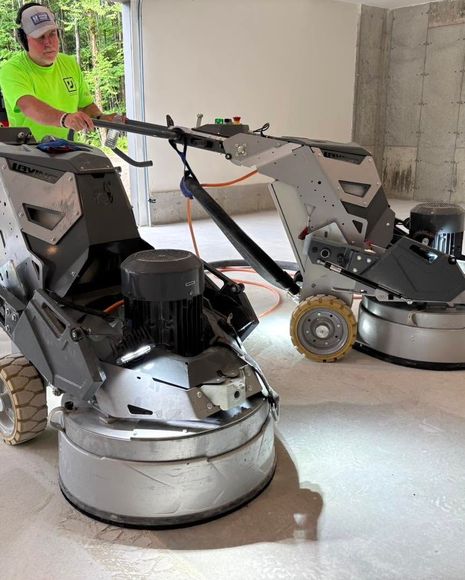 Person operating two floor grinders in an unfinished room
