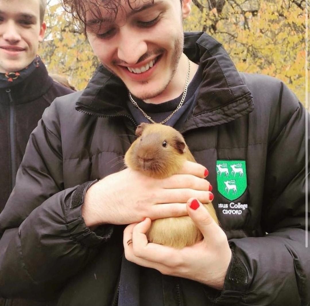 A man in a black jacket holds a guinea pig