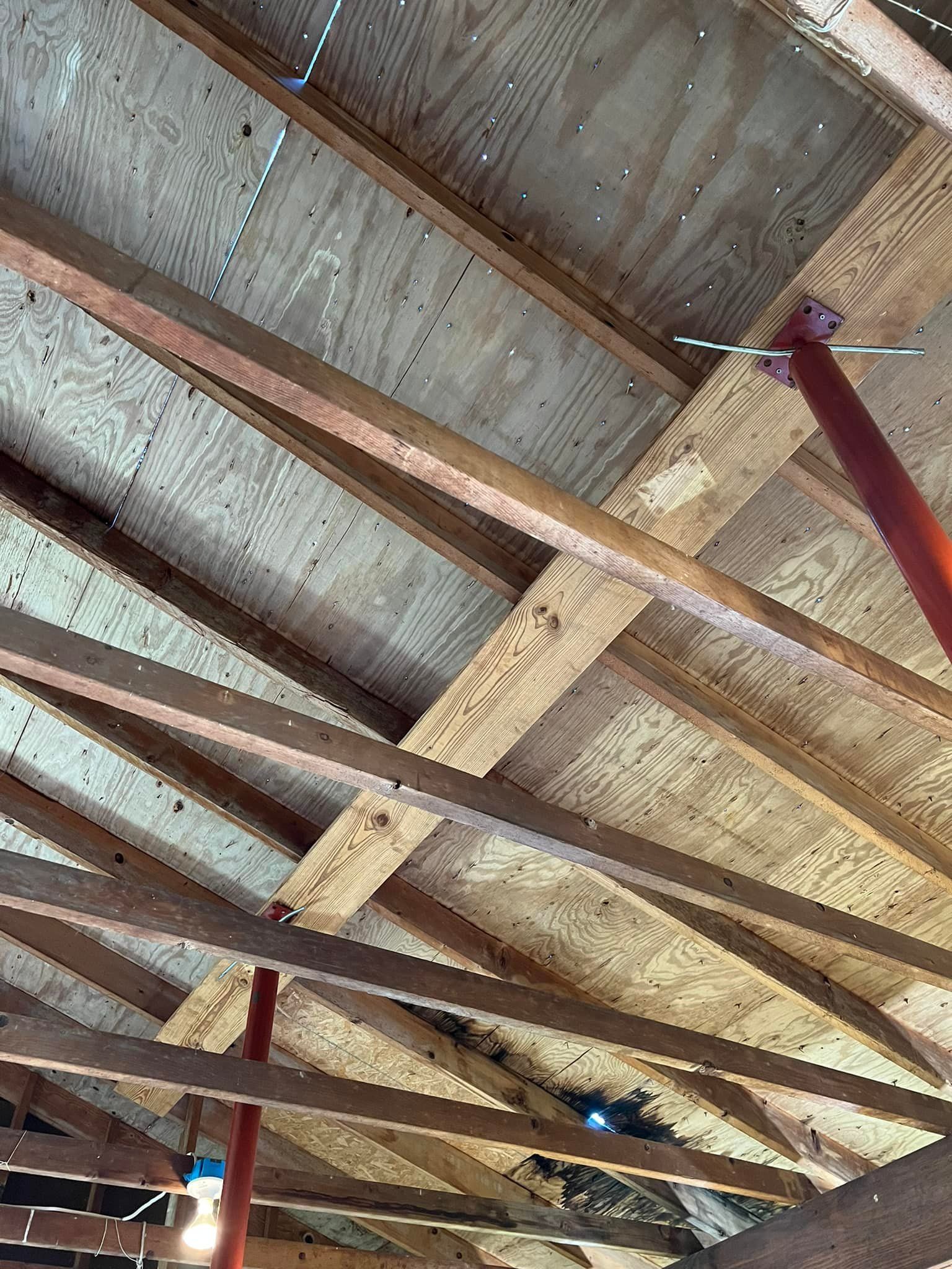 View of a partially exposed ceiling structure with wooden beams and plywood, supported by red adjustable poles.