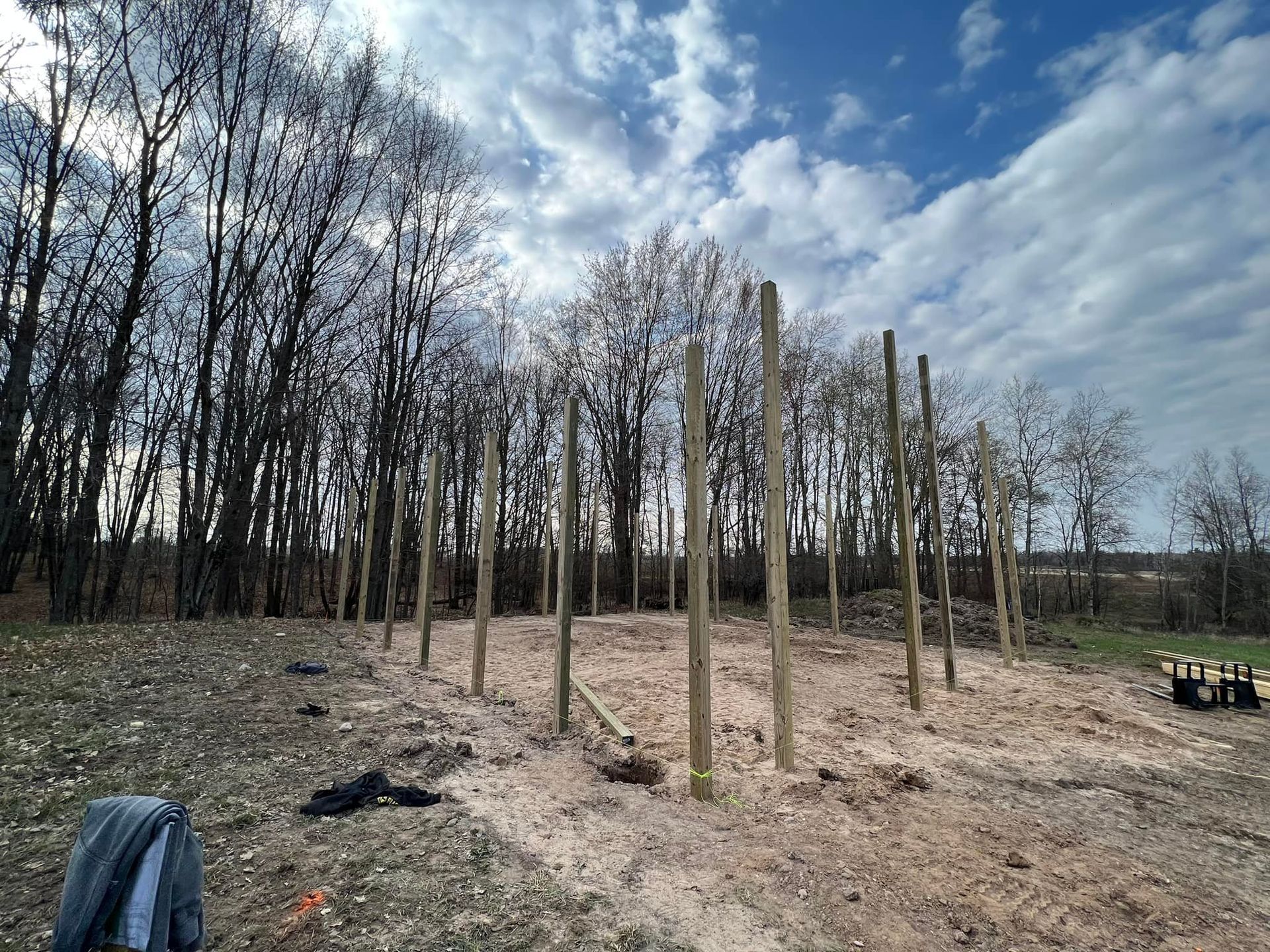 Wooden posts set in the ground, forming a structure in a wooded area, sawdust on the ground.
