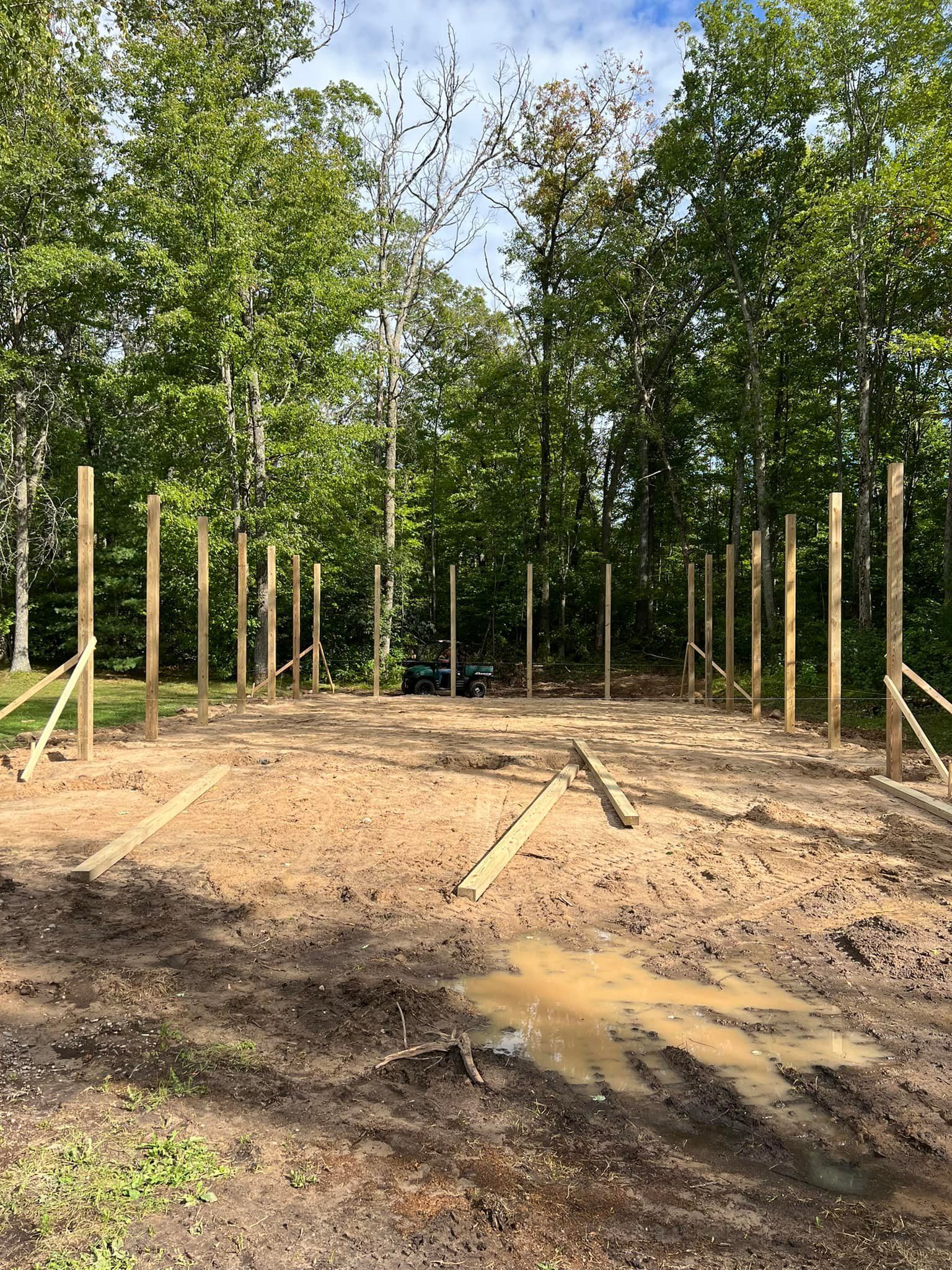 Wooden posts set in dirt, with supporting braces. Trees in the background. Construction site.