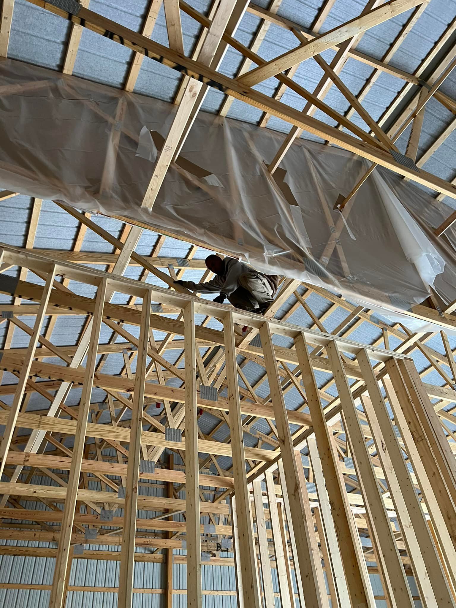 Worker framing wooden roof structure, standing on interior wall frame.