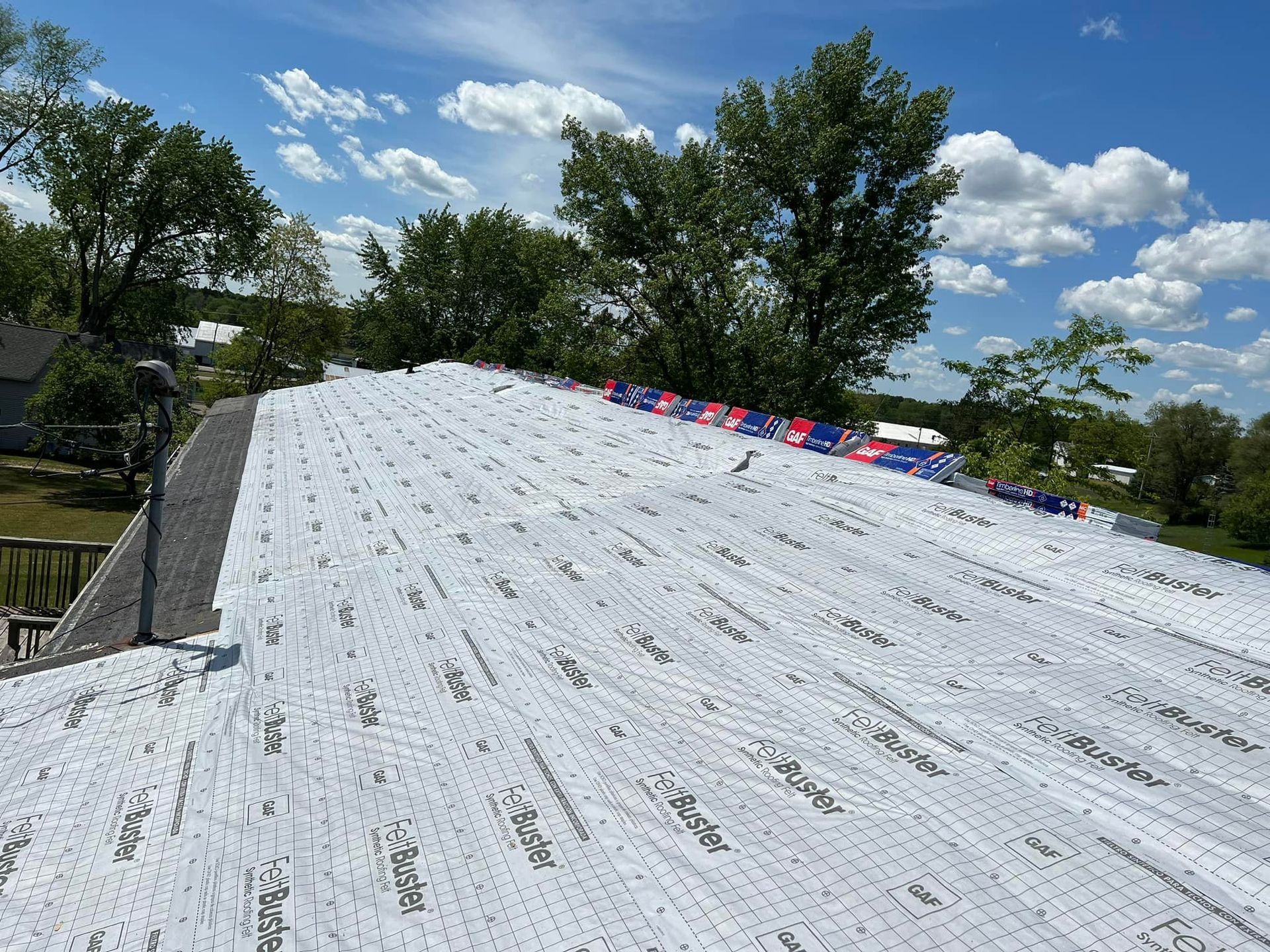 White roofing material covering a roof with blue sky and trees in the background.