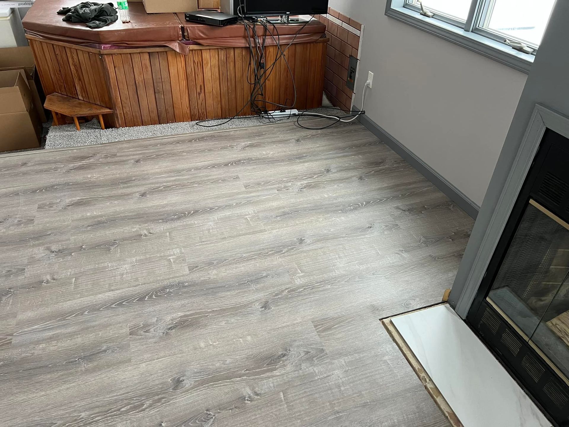 Living room with new wood-look flooring, fireplace, and a wooden cabinet. Boxes are present, indicating a move.