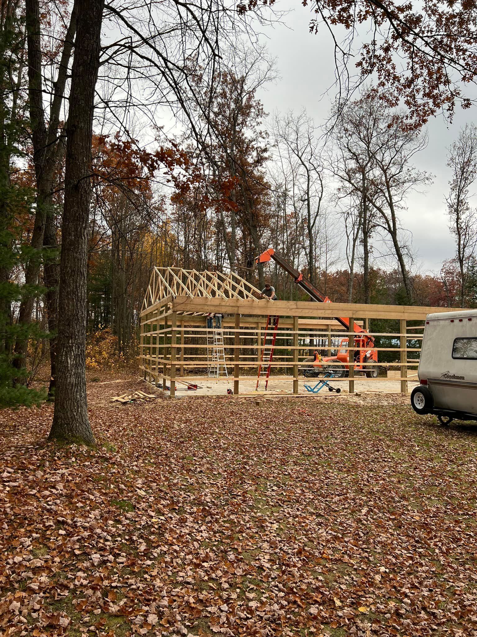 Construction of a wood-framed building in a wooded area; a crane lifts roof components.