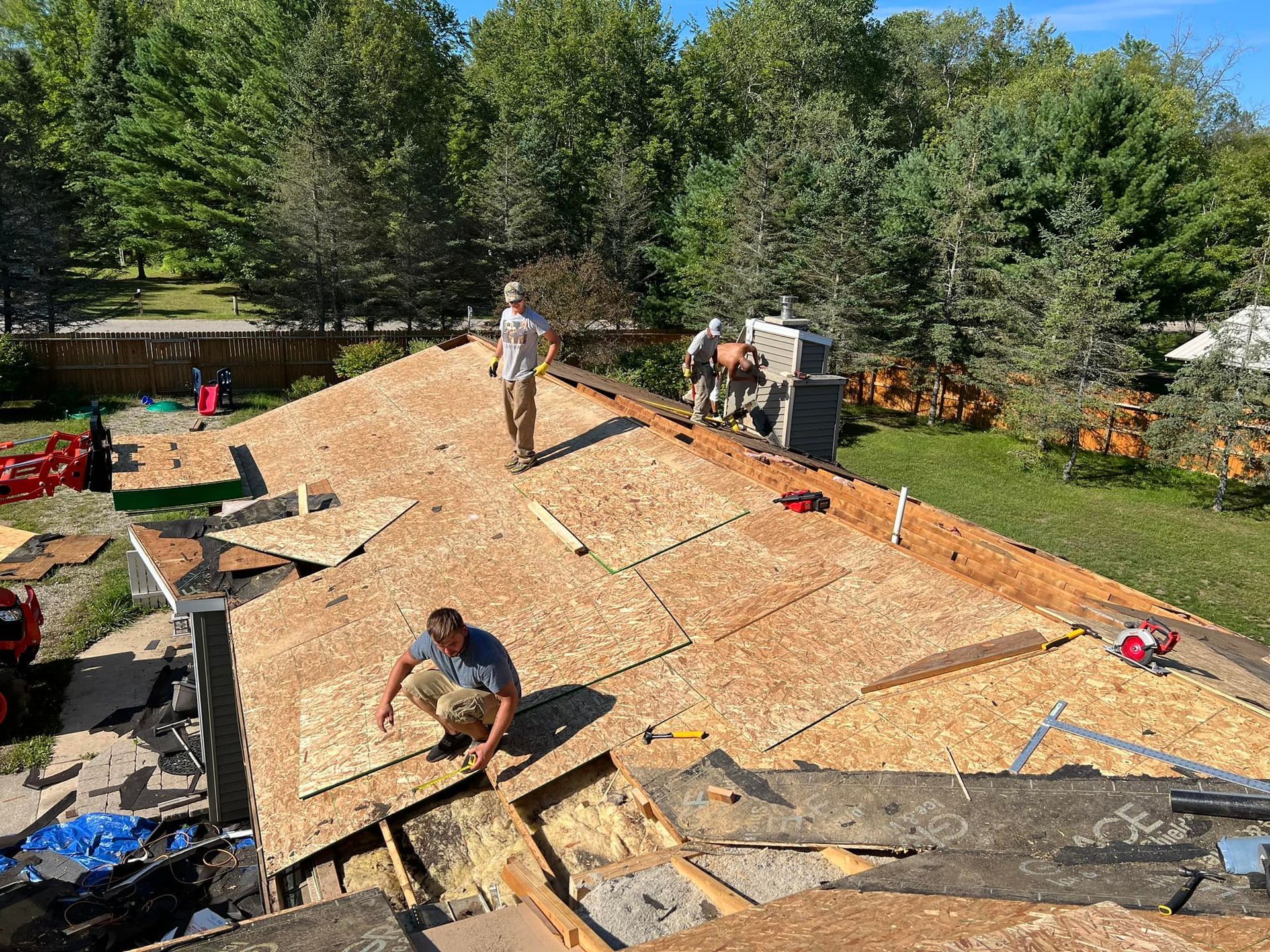 Roofers replacing a roof on a house with plywood and tools under a sunny sky.