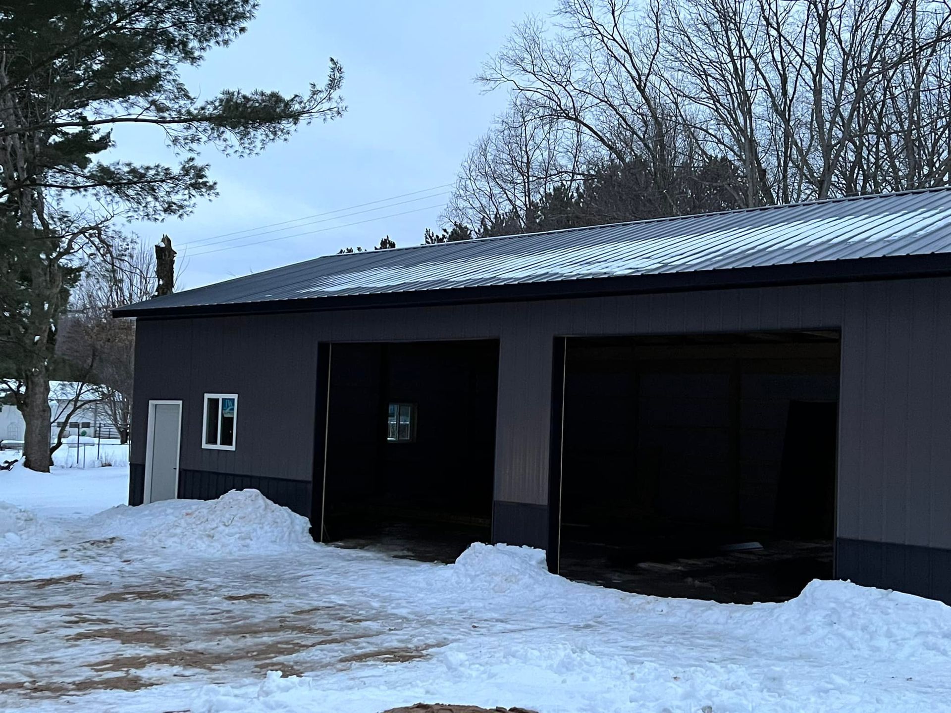 Gray building with two open garage doors, snow on the ground.