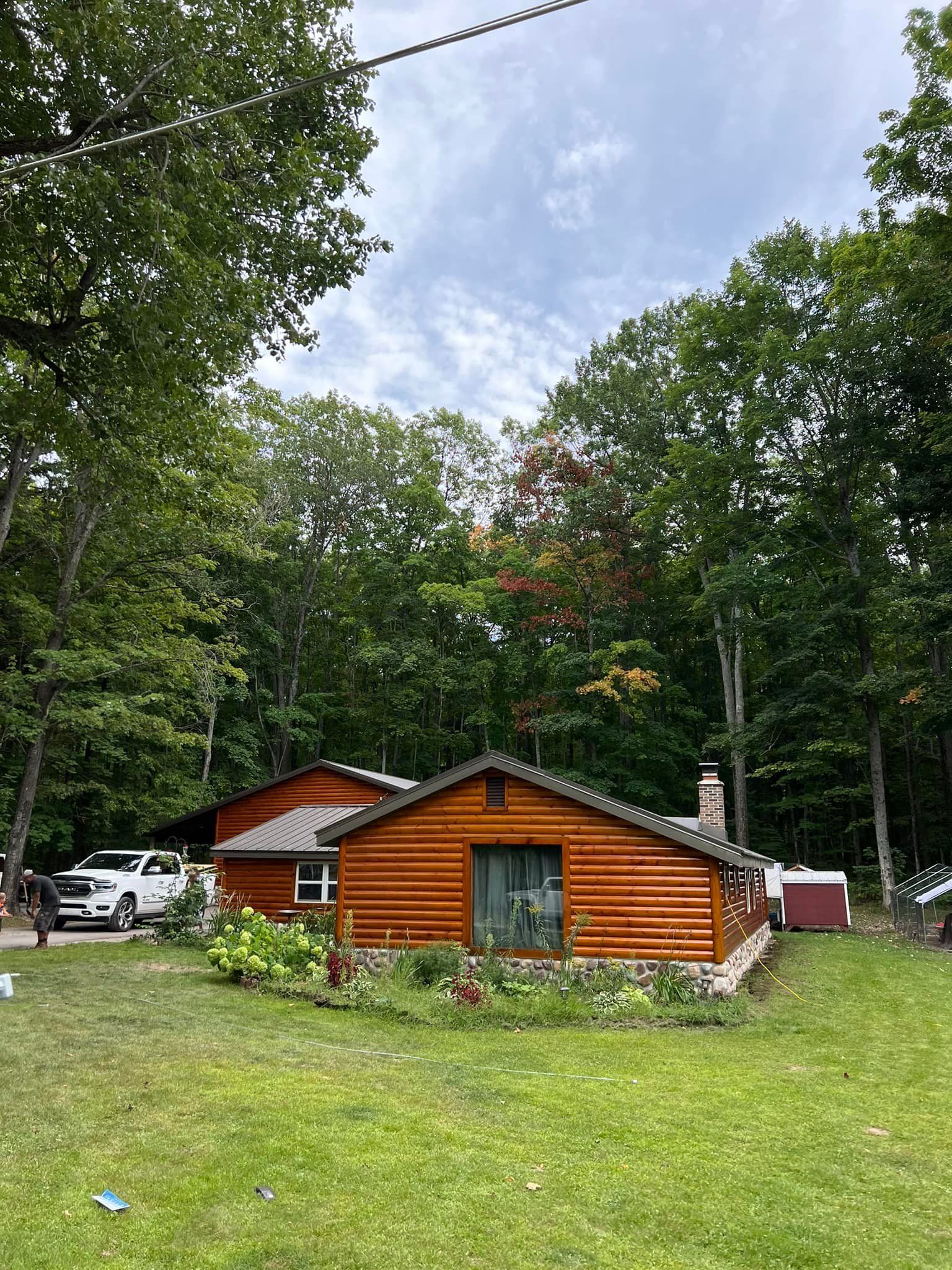Wooden cabin with a lawn surrounded by trees and a cloudy sky.