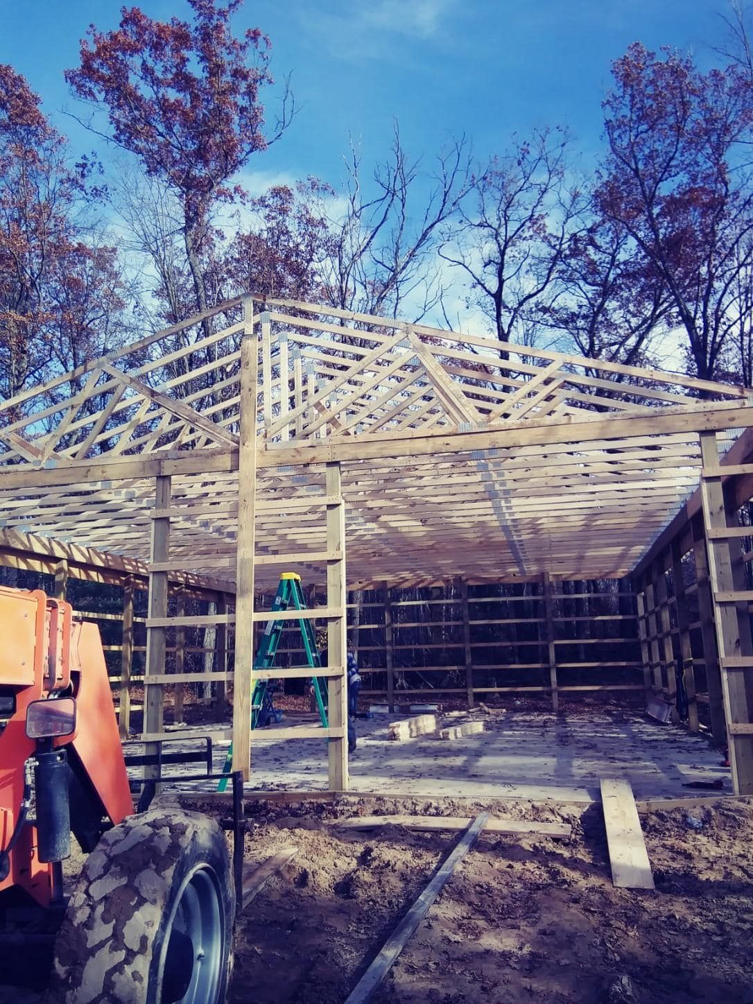 Construction of a wooden building with a partially built roof, outdoors under a blue sky.
