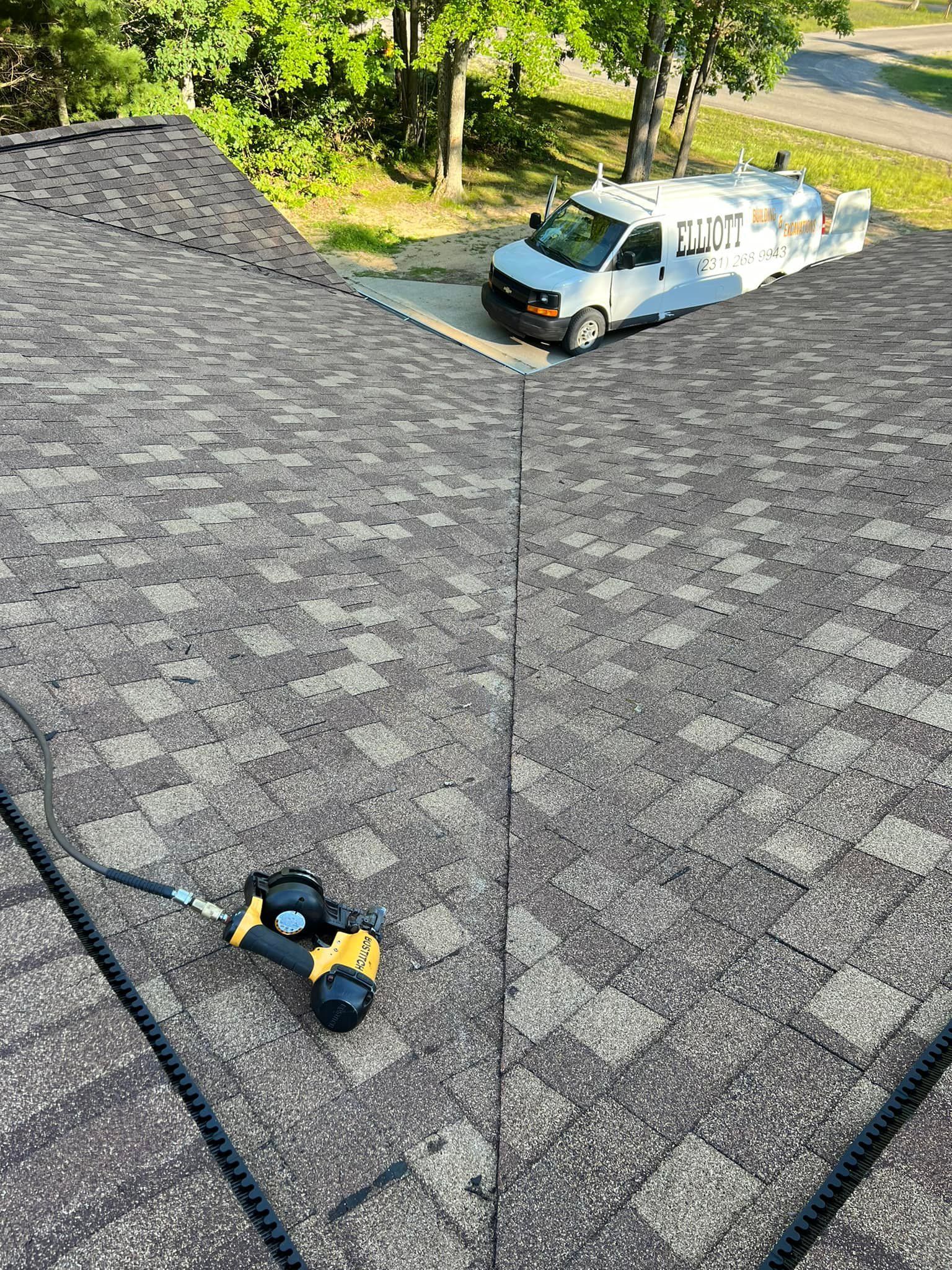 Rooftop with installed asphalt shingles, air nailer, and a work van.