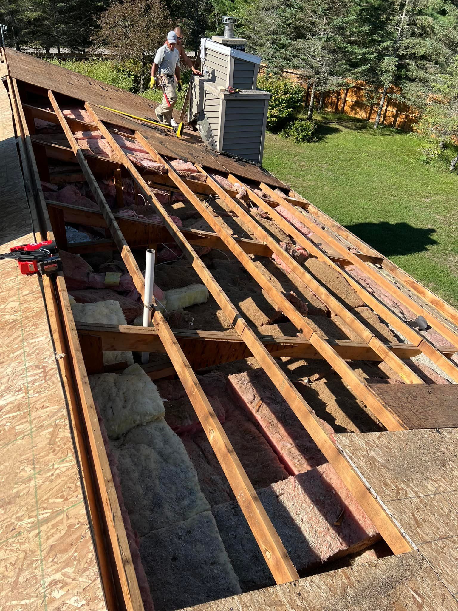 Roofer on a partially torn-off roof. Exposed wooden structure, insulation, and chimney visible.