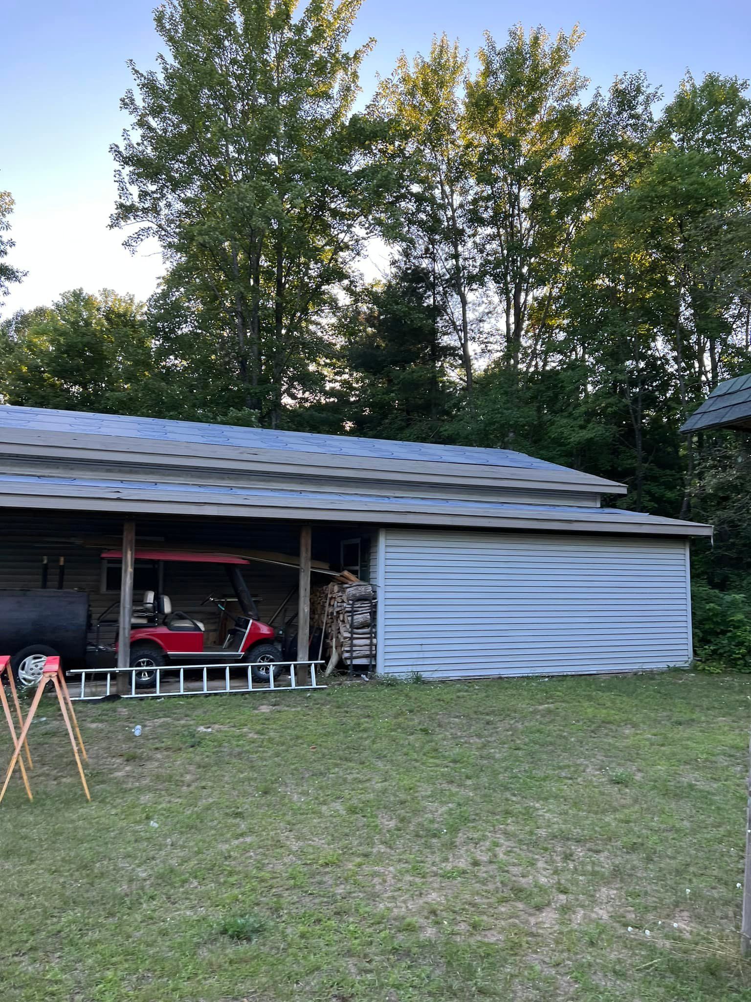 Wooden shed with a red golf cart inside, surrounded by trees and a grassy yard.