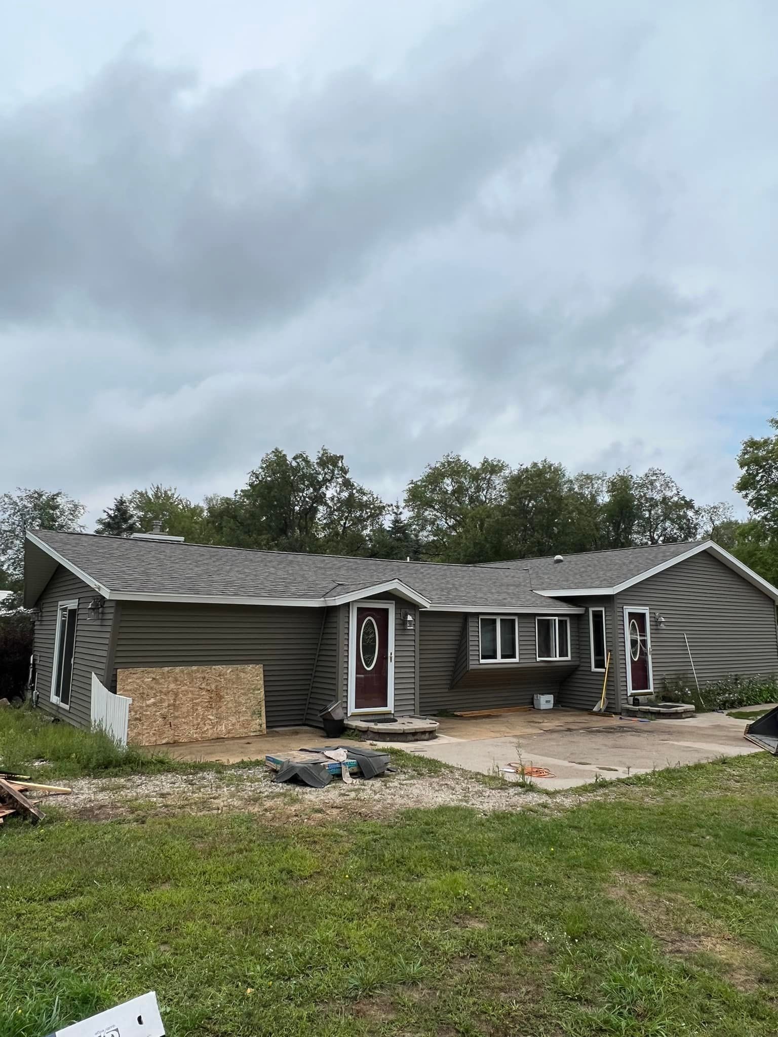 House with roof damage, green siding, and brown doors under a cloudy sky.