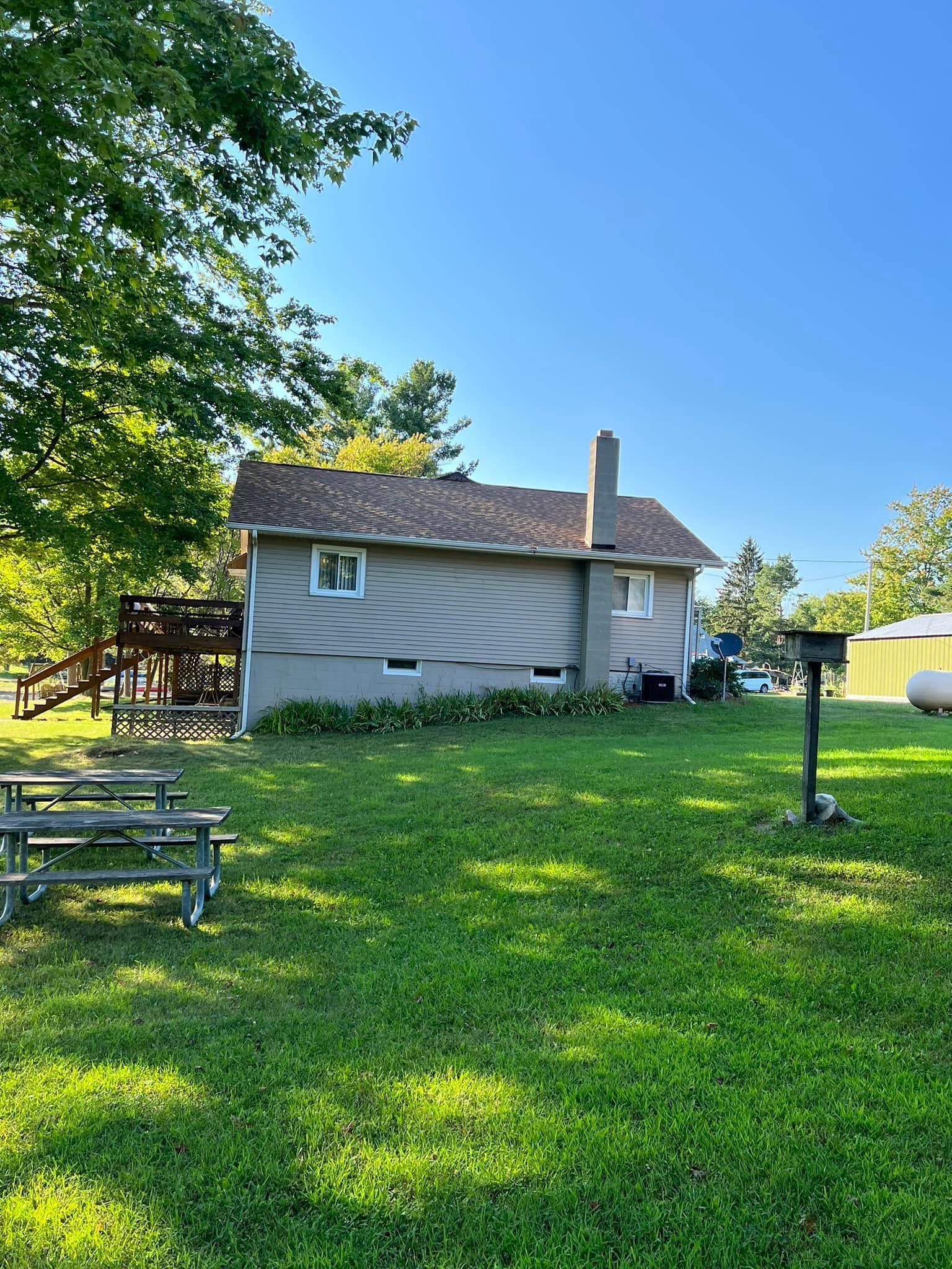 A two-story building with a chimney on a grassy lawn with picnic tables. Sunny day.