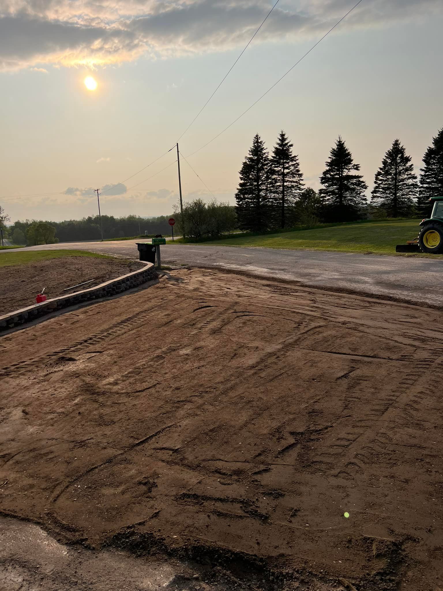Dirt and gravel area with sun overhead, trees, and birds in the sky.