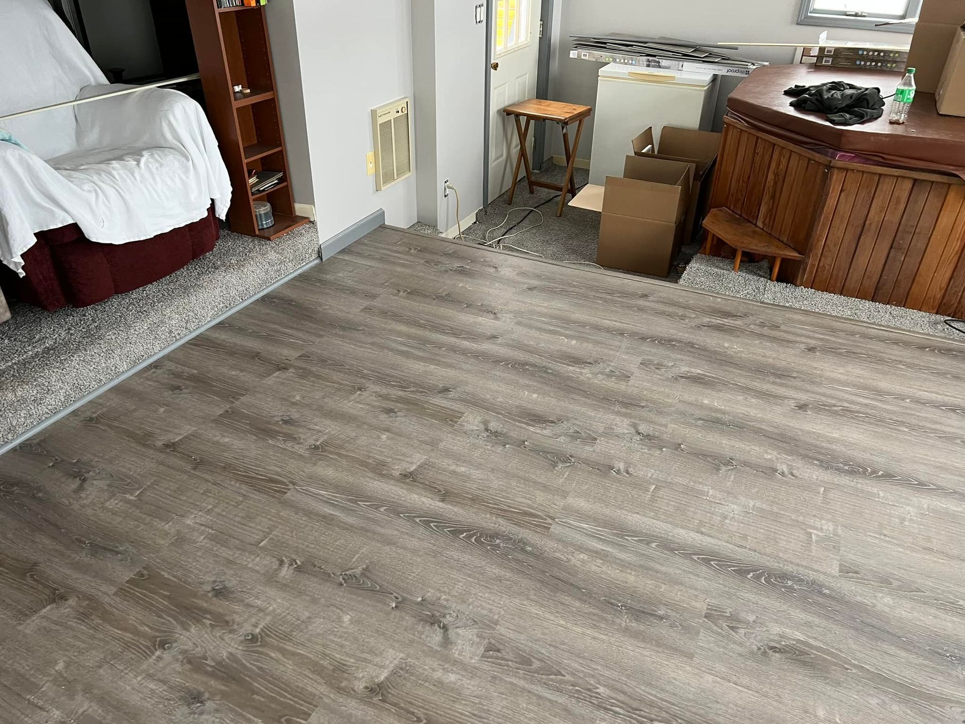 Newly installed wood-look flooring in a room with a bar, furniture, and boxes.