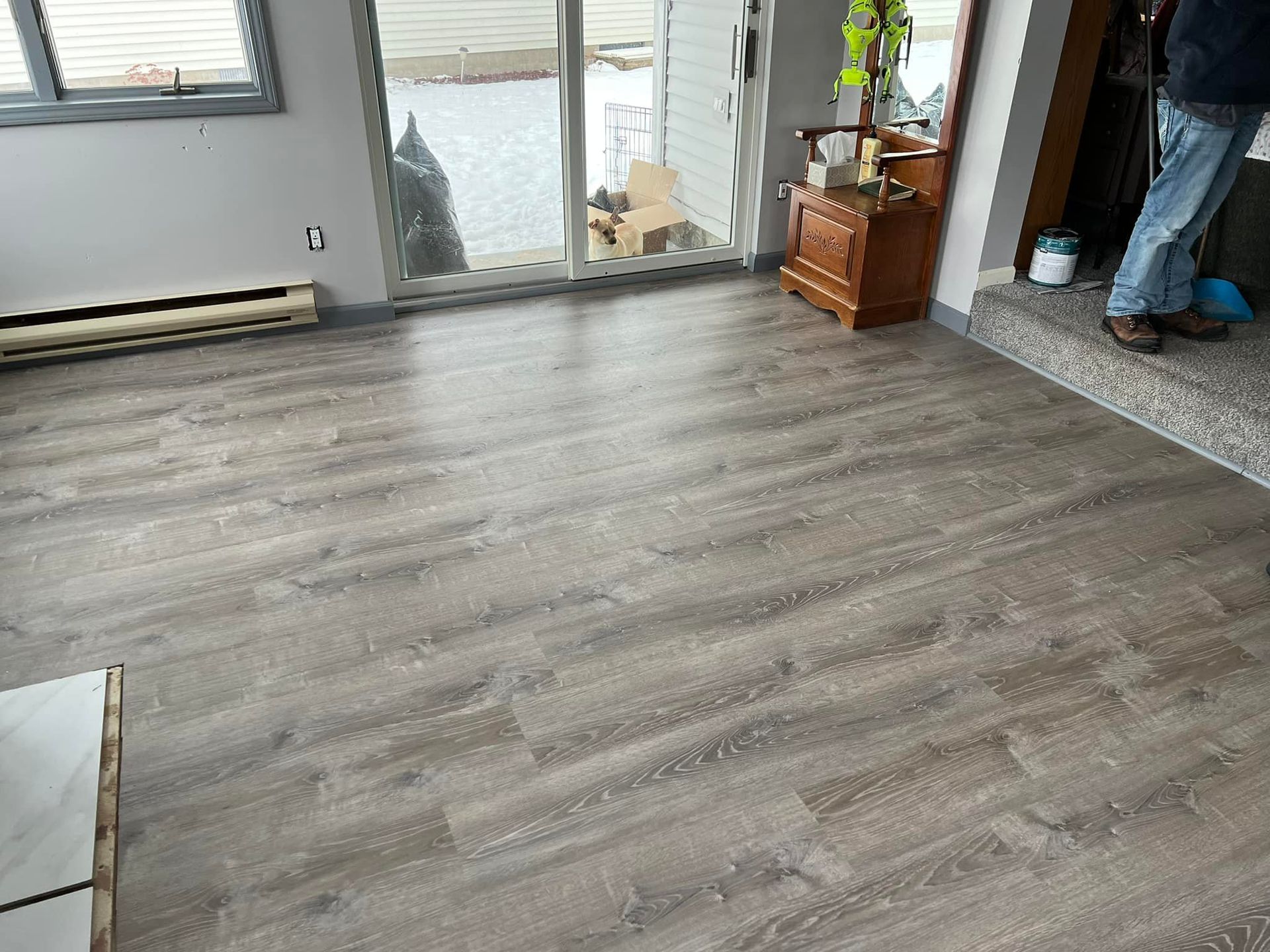 Living room with gray wood-look flooring, large glass door, and a person standing by a fireplace.