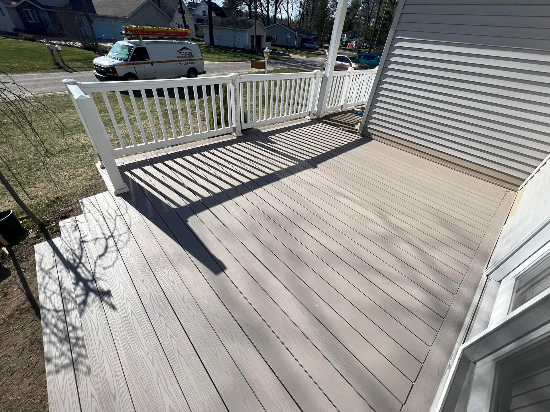 A wooden deck with white railing, and stairs. A white van is in the background.
