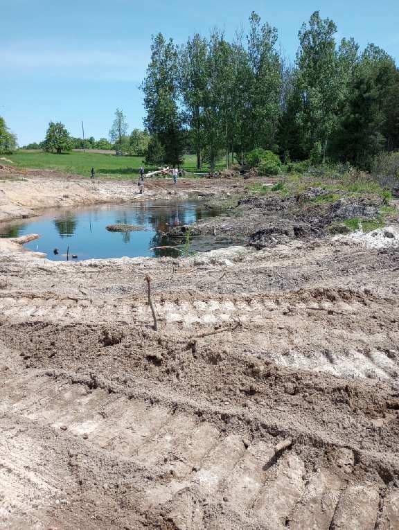 Construction site with a partially filled pond and surrounding dirt.