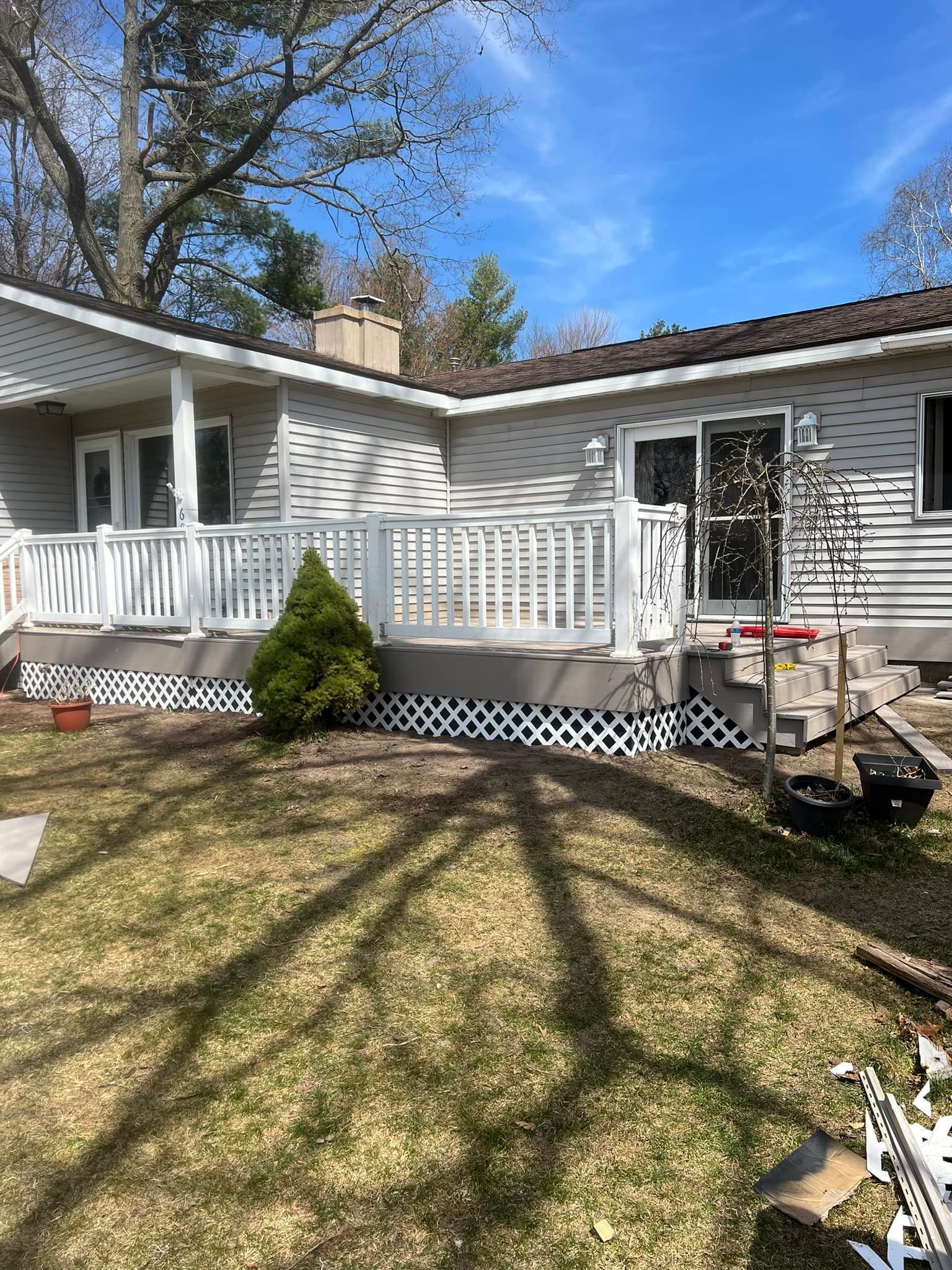 White deck with white railing attached to a beige house, with a small green tree and brown lawn.