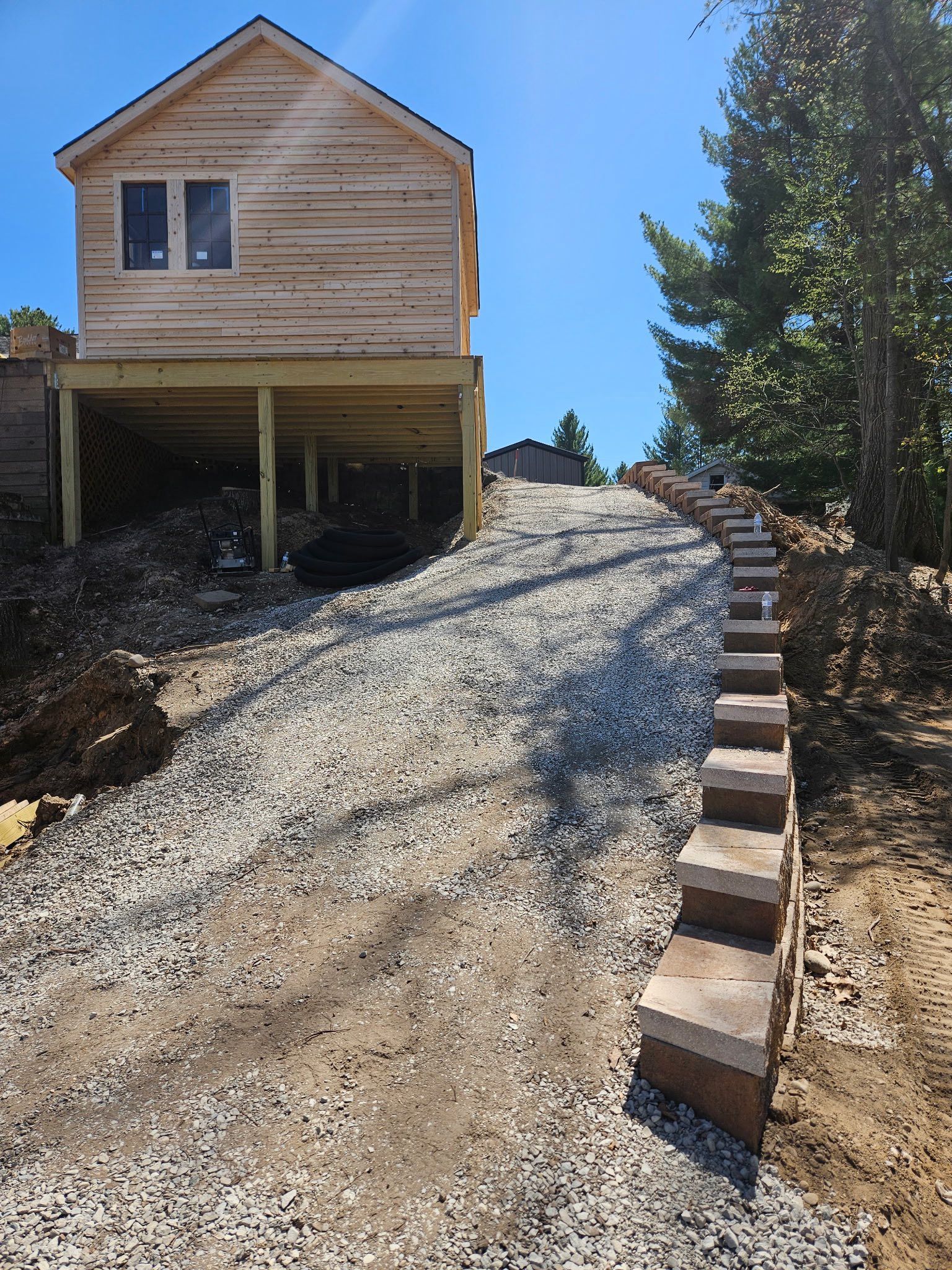 Wooden house on stilts with stone stairs and gravel pathway leading uphill.