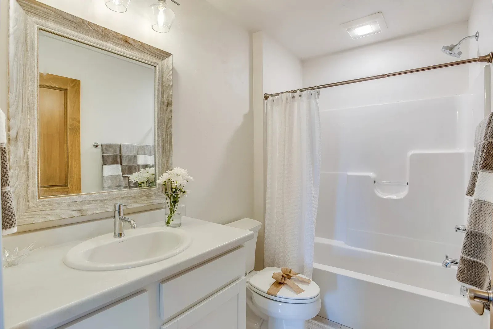 Bathroom with white walls, vanity, and bathtub. Rustic mirror frame, white toilet, and towels.