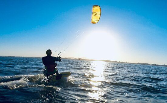 Um homem pratica kitesurf no oceano ao pôr do sol.