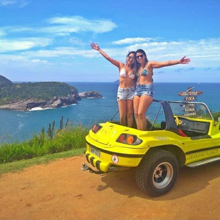 Duas mulheres de biquíni estão em cima de um veículo amarelo com vista para o oceano