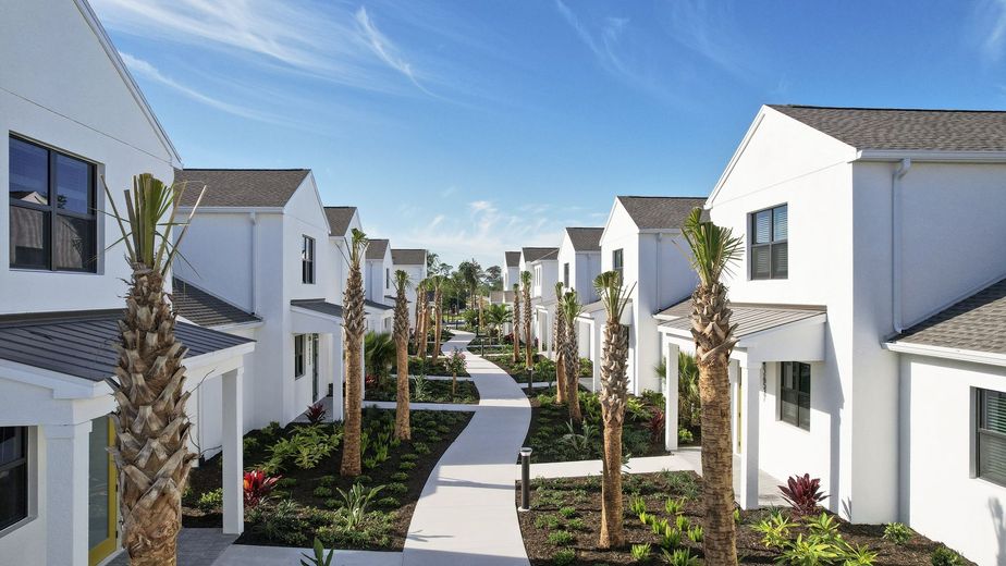 A row of white houses with palm trees and a walkway between them.