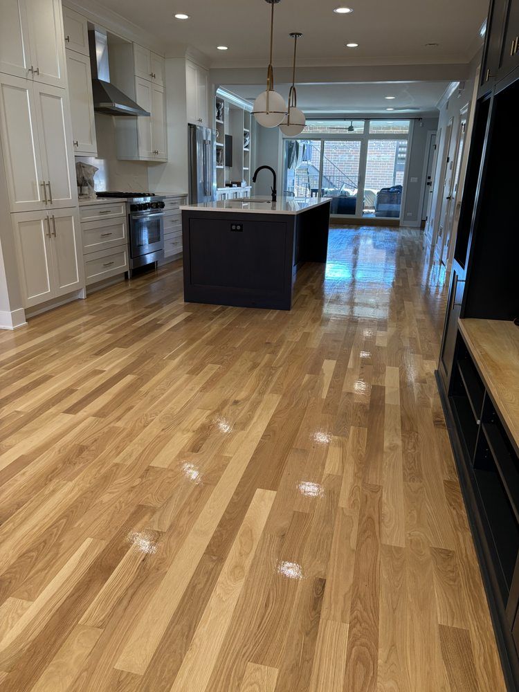Hardwood floors lead through a modern kitchen with white cabinets and a dark island.