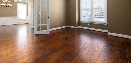 Empty room with dark wooden floors, brown walls, and white trim and window.