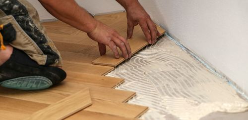 Person installing wood flooring, applying adhesive to the subfloor.
