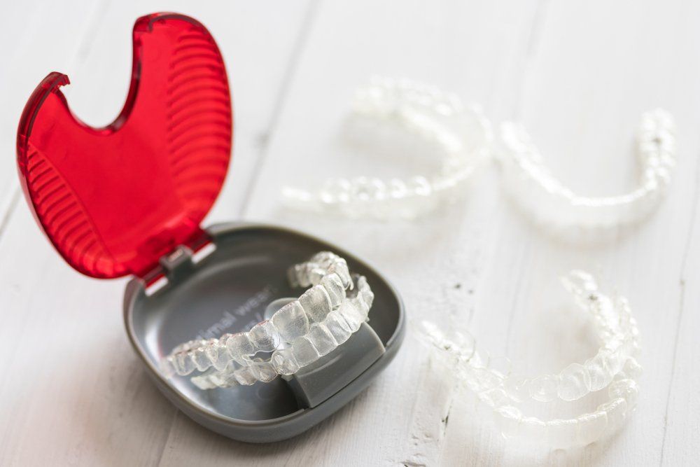Clear aligners in a red and gray case with additional aligners on a white surface.