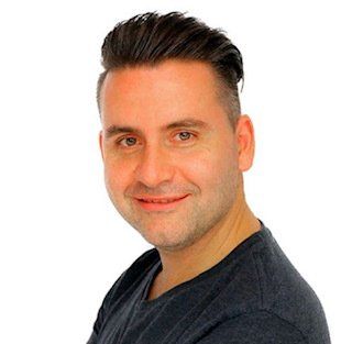 Man with dark hair and a gray t-shirt, smiling at the camera against a white background.