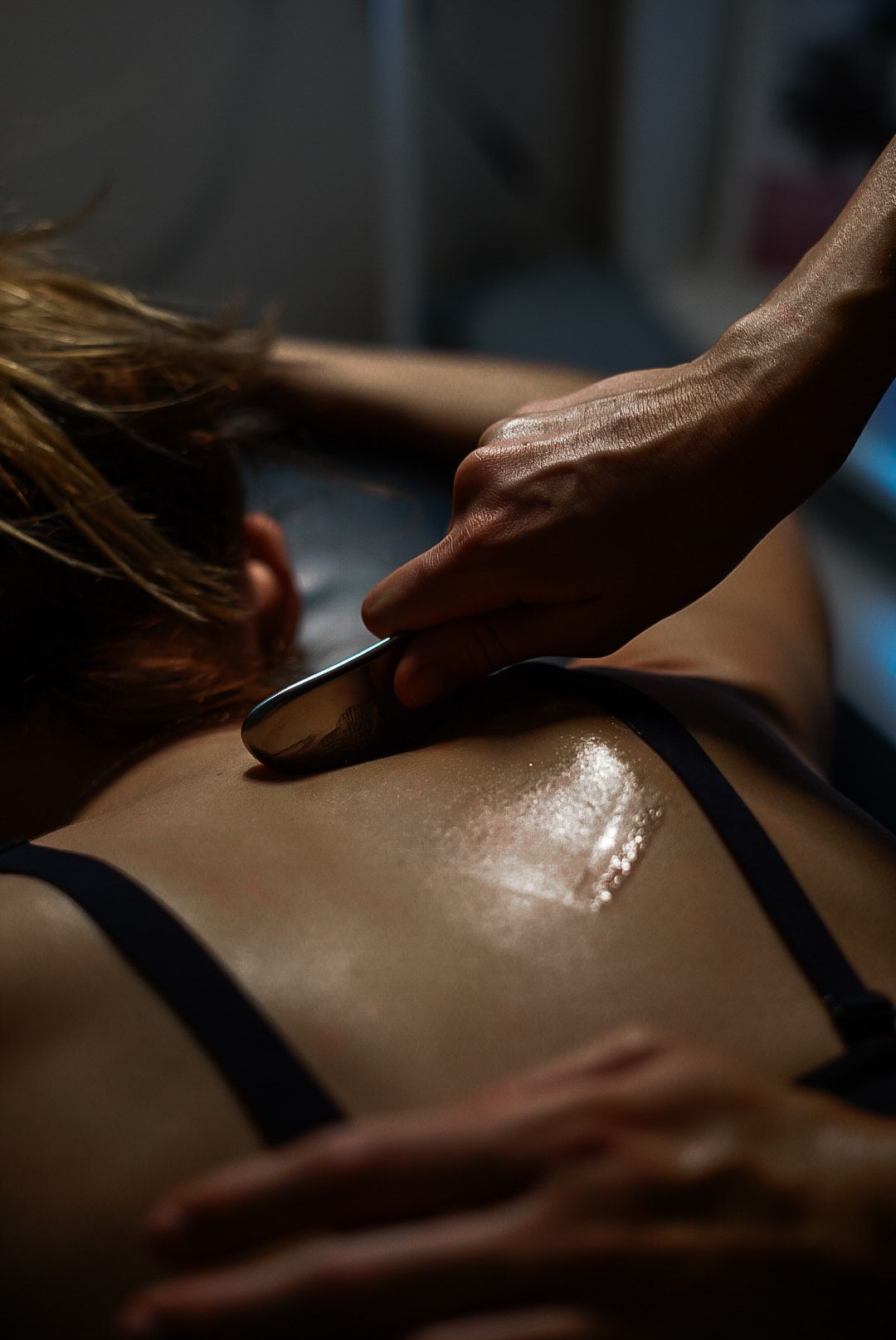 Person receiving a gua sha treatment on their back. Hand using tool on oiled skin.
