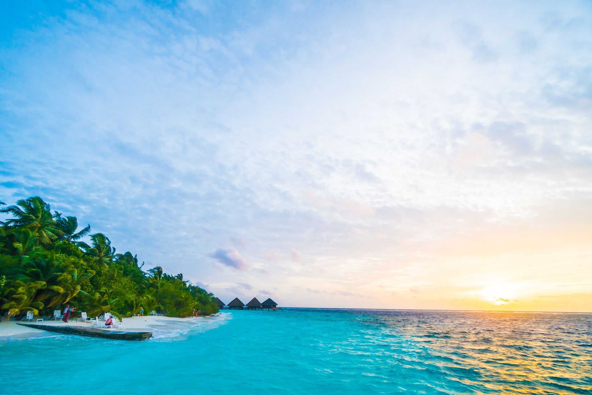 A sunset over a tropical beach with palm trees and a boat in the water.