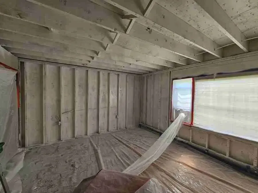 Interior of a partially finished room with exposed insulation, a hammock, and a window on the right.