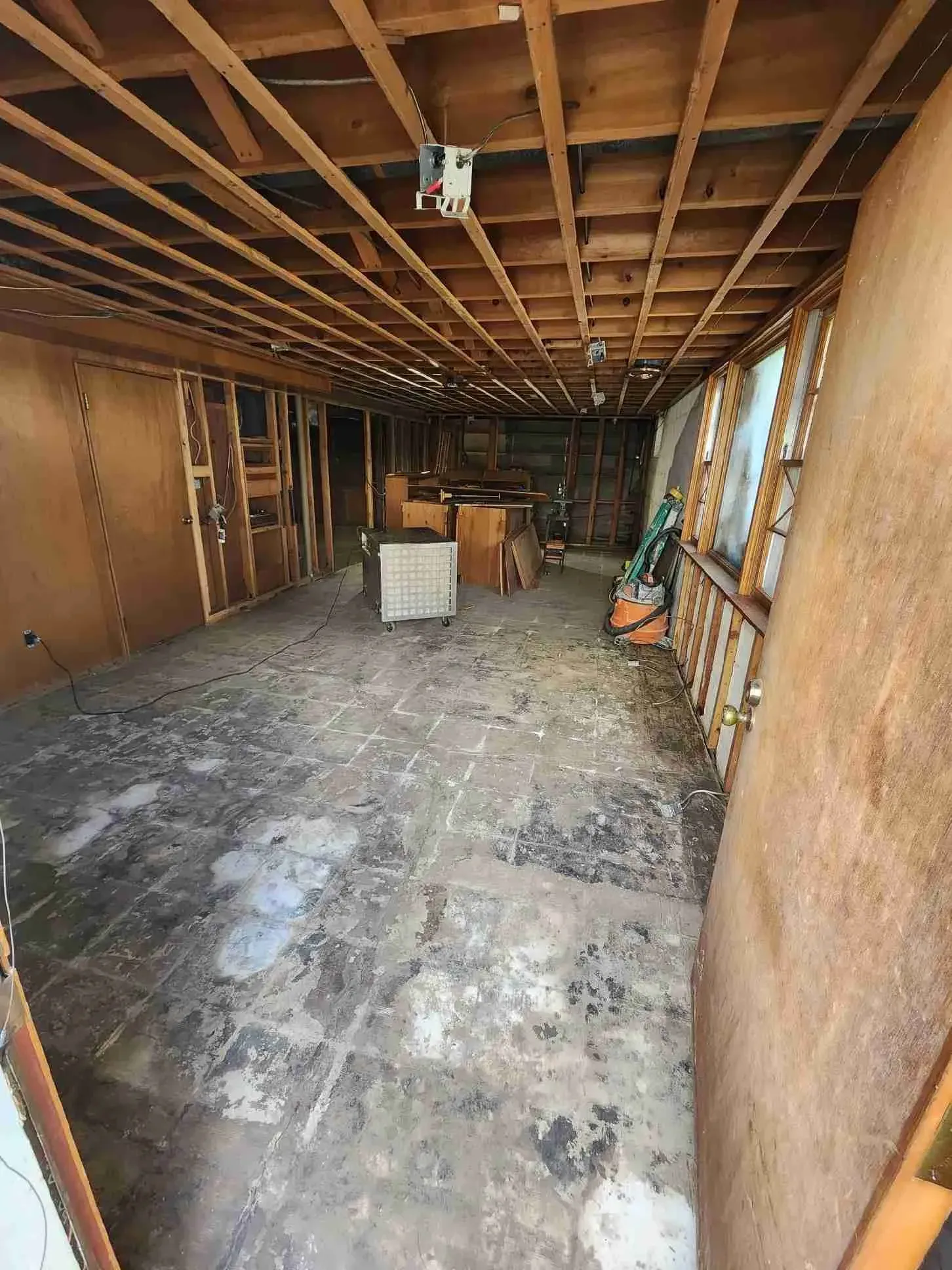 Empty unfinished garage with exposed wooden beams, concrete floor, and scattered construction materials.