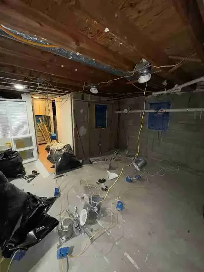 Partially demolished room with exposed ceiling beams, debris on the floor, and blue-covered windows