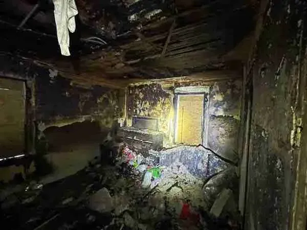 Burned, debris-filled room with charred walls and a bright yellow door or window