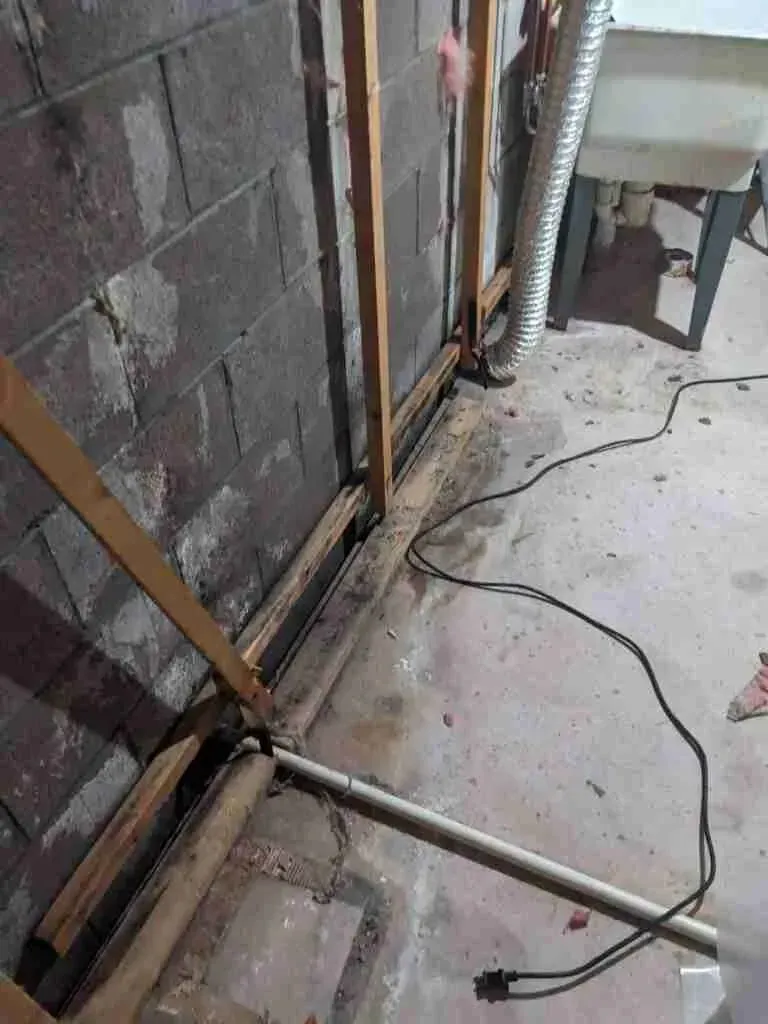 Exposed pipes and electrical cord along a cinder block wall in a construction area