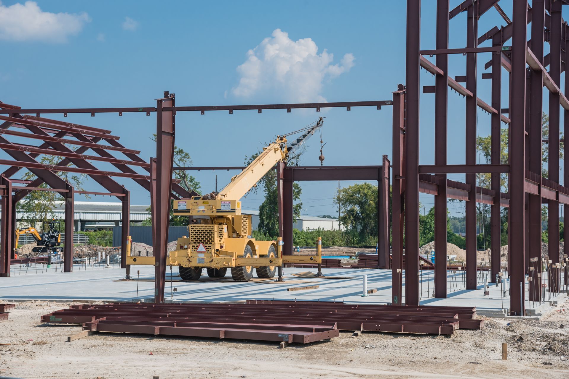 Construction site with steel frame beams and a yellow crane under a clear blue sky