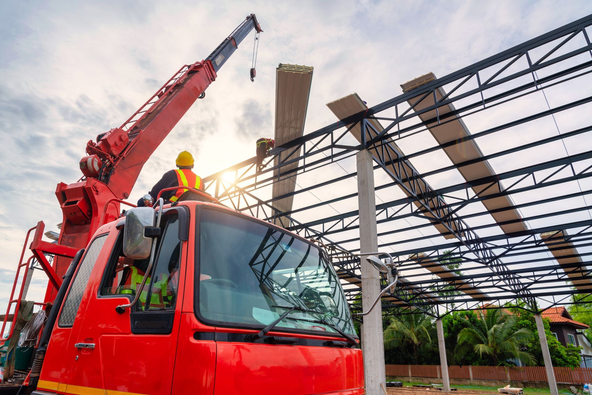 Red crane lifting steel beams during construction beside a partially built structure
