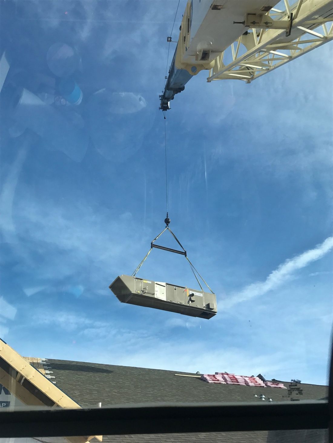 Crane hoisting a large rectangular object above rooftops against a blue sky